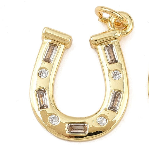 Gold horseshoe charm with alternating baguette and round clear crystals, featuring a top jump ring on a white background.