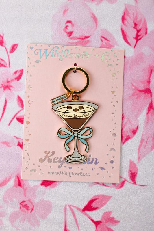 An espresso martini Wildflower keychain with a light blue bow charm, shown on a pink backing card.