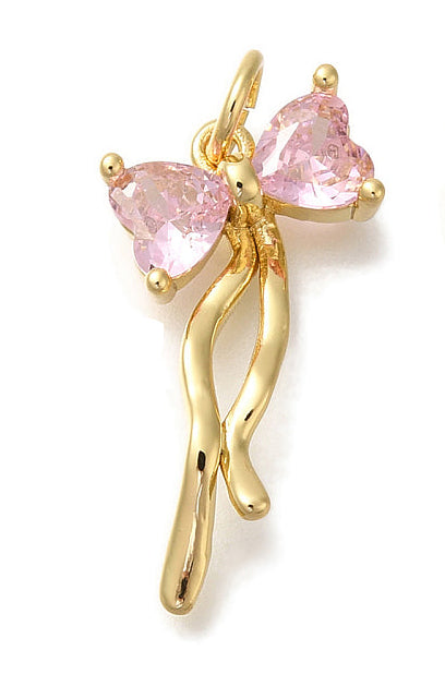 Gold pink bow charm featuring two pink heart-shaped stones in a gold-tone setting with flowing metal ribbons.
