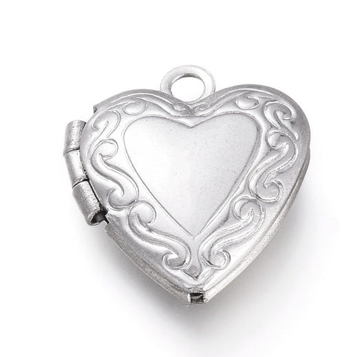 Silver heart locket charm featuring a textured scrollwork border around a smooth center, complete with a side hinge and top loop.